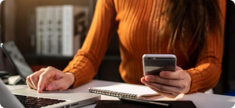 Mulher sentada em uma mesa usando smartphone e notebook